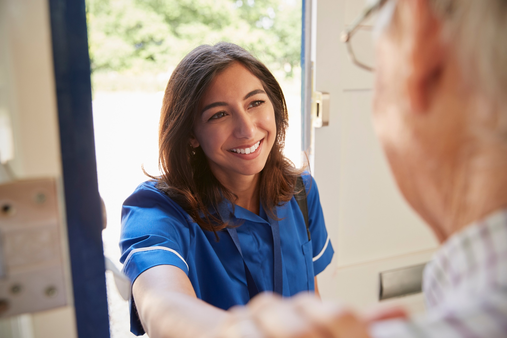 Nurse on home visit greeting senior man, over shoulder view